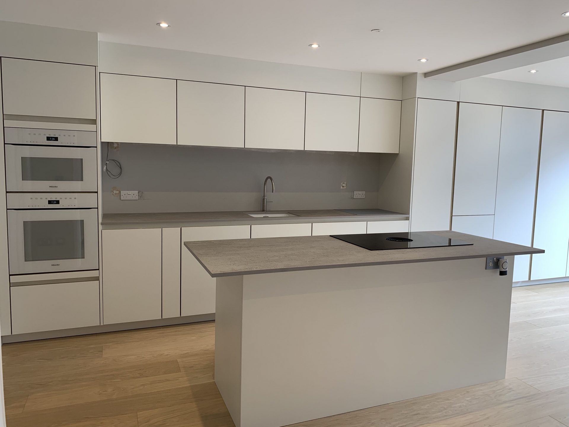Modern Kitchen with White Appliances and Grey Splashback. High Gloss White Doors. TImber flooring throughout the dining room and kitchen space.